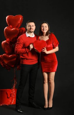 Happy couple in love with gift and balloons on black background. Valentine's Day celebration