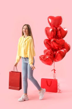 Young woman with paper bag and balloons on pink background. Valentine's Day celebration