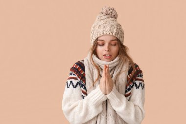 Frozen young woman in winter clothes on beige background