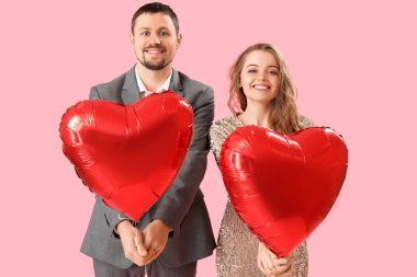 Pembe arka planda kalp şeklinde balonları olan mutlu genç bir çift. Sevgililer Günü kutlaması