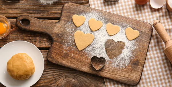 Raw heart shaped cookies, dough and heart shaped mold on wooden background. Valentines Day celebration