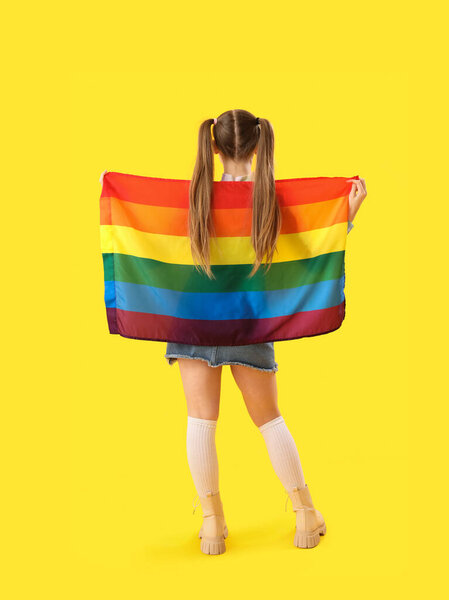 Красивая молодая женщина с флагом ЛГБТ на желтом фоне, вид сзади