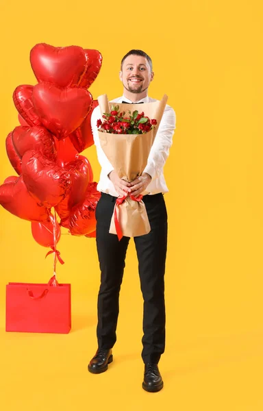 Handsome man with roses and balloons on yellow background. Valentine\'s Day celebration