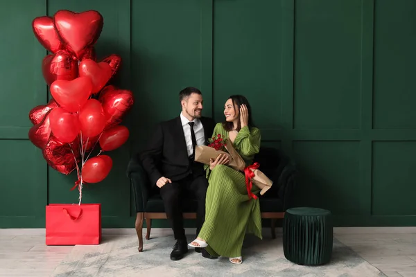 Happy couple in love with roses sitting on sofa near green wall. Valentine\'s Day celebration