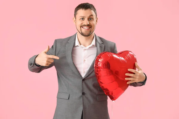 Handsome man with heart-shaped balloon on pink background. Valentine\'s Day celebration