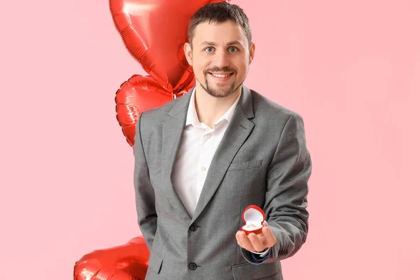 Handsome man with engagement ring and balloons on pink background. Valentine\'s Day celebration