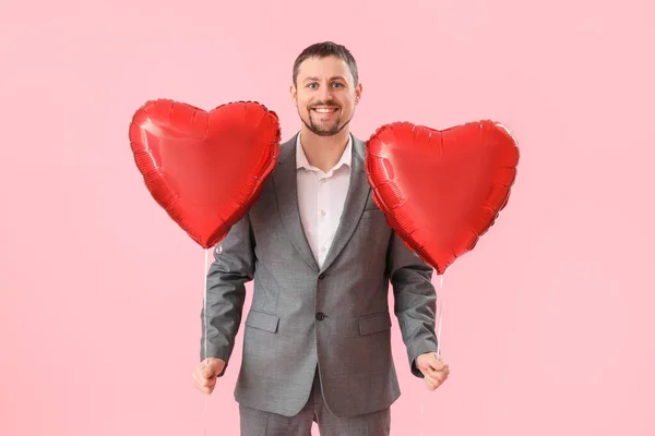 Handsome man with heart-shaped balloons on pink background. Valentine's Day celebration