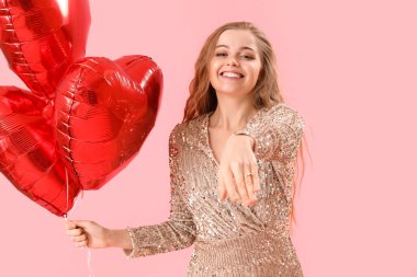 Happy young woman with heart-shaped balloons and engagement ring on pink background. Valentine's Day celebration