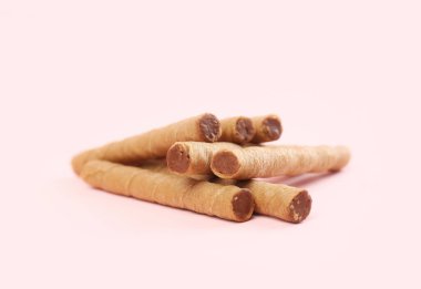 Tasty wafer rolls with boiled condensed milk on pink background
