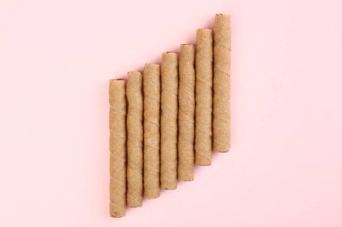 Tasty wafer rolls on pink background