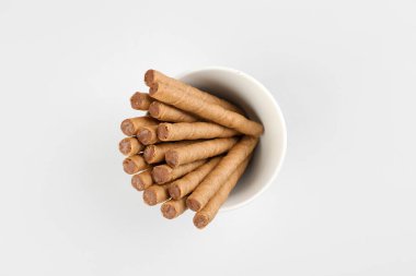 Bowl of tasty wafer rolls with condensed boiled milk on grey background