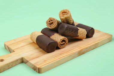 Board with chocolate wafer rolls on green background