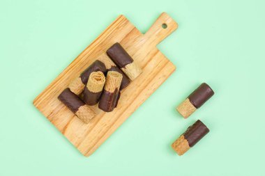 Board with chocolate wafer rolls on green background