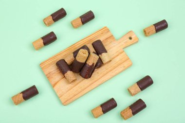 Board with chocolate wafer rolls on green background