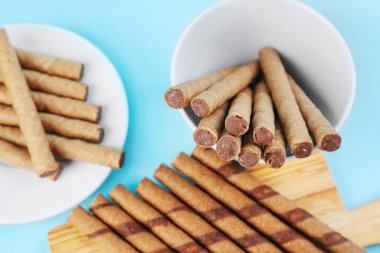 Plate, bowl and board with tasty wafer rolls on blue background