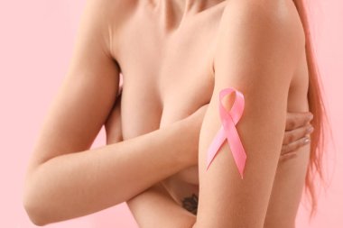 Naked young woman with pink ribbon on color background, closeup. Breast cancer awareness concept