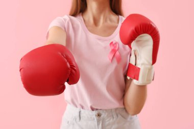Young woman in boxing gloves with pink ribbon on color background. Breast cancer awareness concept