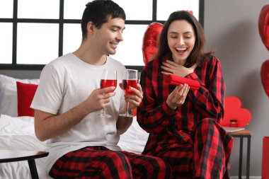 Young woman opening gift from her husband in bedroom on Valentine's Day