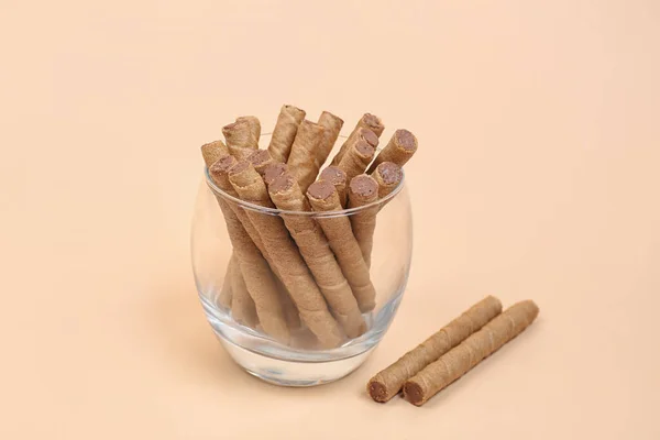 Glass of tasty wafer rolls with boiled condensed milk on beige background