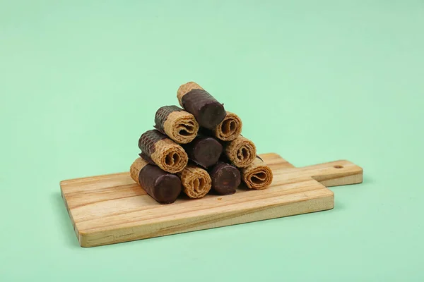 Board with chocolate wafer rolls on green background