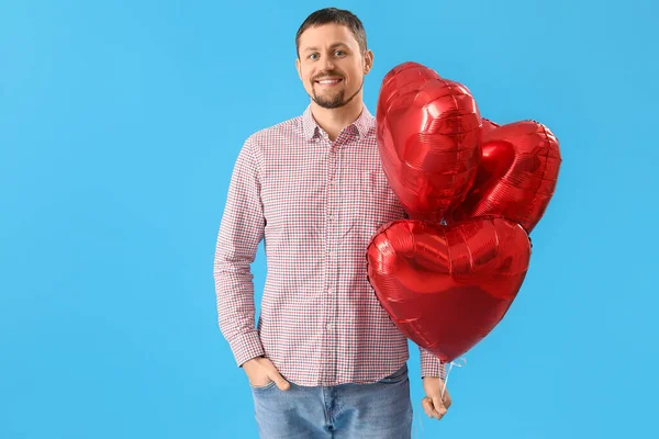 Handsome man with heart-shaped balloons on light blue background. Valentine\'s Day celebration