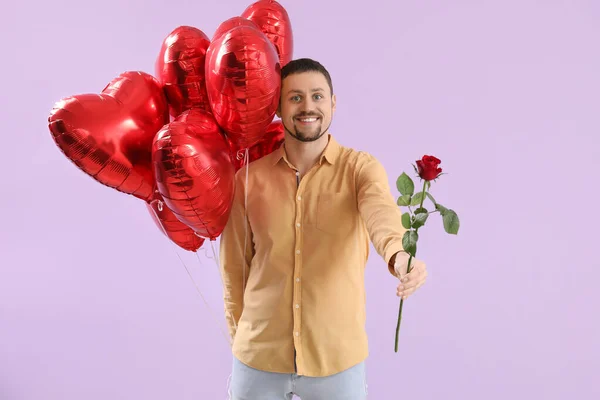 Handsome man with heart-shaped balloons and rose on lilac background. Valentine\'s Day celebration