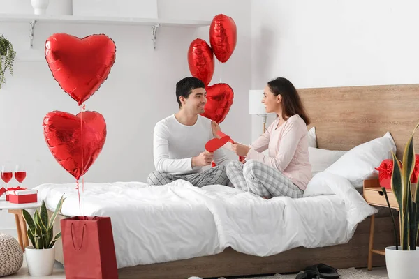 Young couple with paper hearts in bedroom on Valentine\'s Day