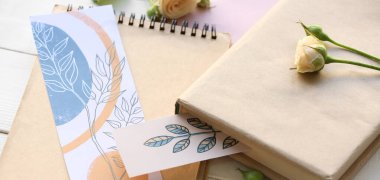 Book, notebook, stylish bookmarks and flowers on light table