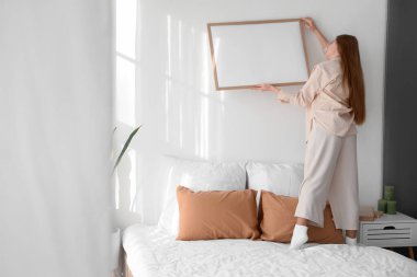 Yatak odasındaki ışık duvarına boş bir çerçeve asan genç bir kadın.