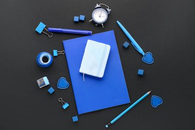 Set of blue stationery with notebooks and alarm clock on dark background