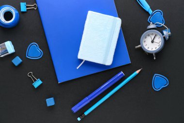 Set of blue stationery with notebooks and alarm clock on dark background