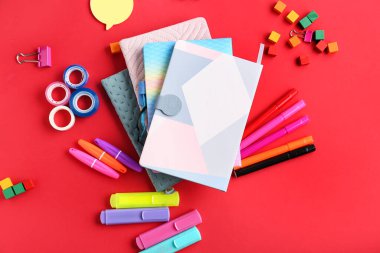 Stack of notebooks and different stationery on red background