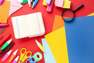 Composition with different stationery and open notebook on red background
