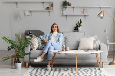 Young woman sitting on grey couch at home
