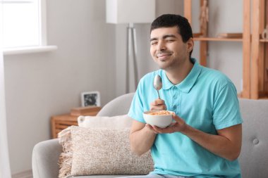 Happy young man with spoon and bowl of cornflakes at home