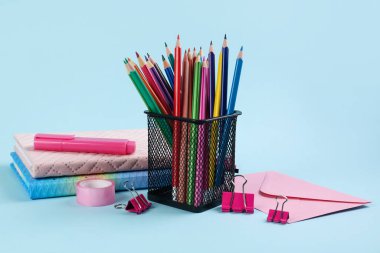 Holder with pencils, notebooks and stationery on blue background