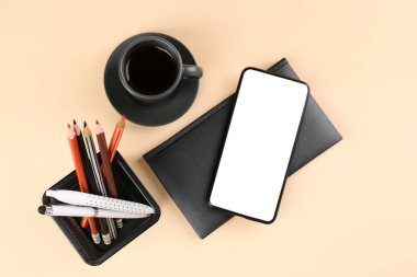Stationery holder, mobile phone, notebook and cup of coffee on beige background