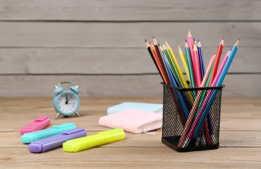 Pencils holder, markers, notebooks and clock on wooden background