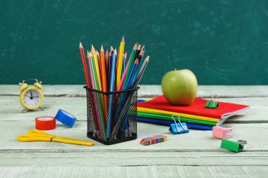 Green apple with notebooks, pencils holder, different stationery and clock on wooden background