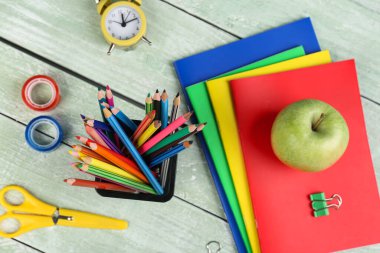 Green apple with notebooks, pencils holder, school stationery and clock on wooden background