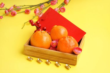 Box with mandarins, red envelope and Chinese symbols on yellow background