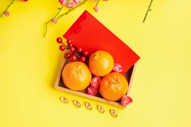 Box with mandarins, red envelope and Chinese symbols on yellow background