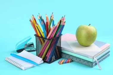 Holder with stationery, notebooks and apple on blue background