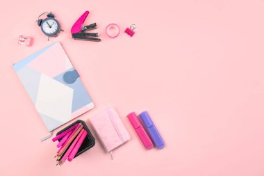 Holder with stationery, notebooks and alarm clock on pink background