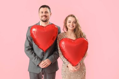 Pembe arka planda kalp şeklinde balonları olan mutlu genç bir çift. Sevgililer Günü kutlaması