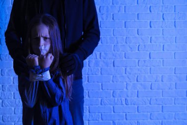 Terrorist and scared little hostage on brick background