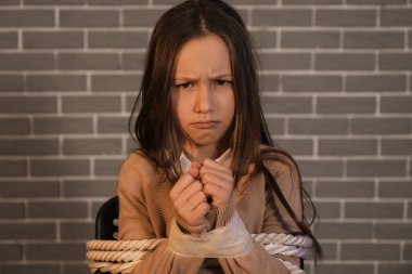 Scared little hostage tied to chair on brick background