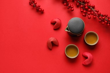 Fortune cookies, teapot, cups of tea and berries on red background. Chinese New Year celebration