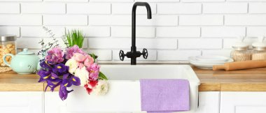 Ceramic sink with beautiful bouquet of fresh flowers in interior of modern kitchen