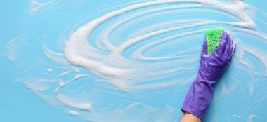 Hand with sponge cleaning light blue surface